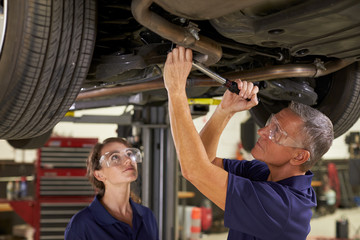 Male And Female Mechanics Working Underneath Car Together