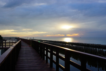 Long simple wooden jetty leading into blue ocean in the gulf of Thailand with sunset