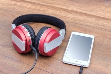 Headphones with mobile phone on wooden table close up