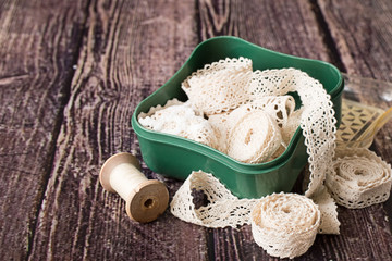  Box with lace ribbons.    Old green box with lace ribbons and reel of thread on a brown wooden table.