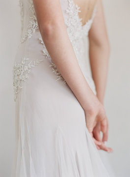 Bride wearing wedding dress, hands behind back, mid section