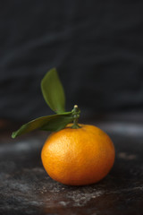 Tangerine. Ripe and delicious tangerine fruit on black metal background with a green leaf.