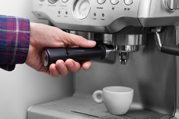 Man is using a tamper to press freshly ground morning coffee into a coffee tablet
