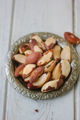 Brazil nuts in metal plate over the white wooden table.