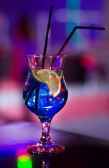 Beautiful glass with a cocktail at the bar on the table. Night club. Alcoholic drink blue color with a lemon on the inside