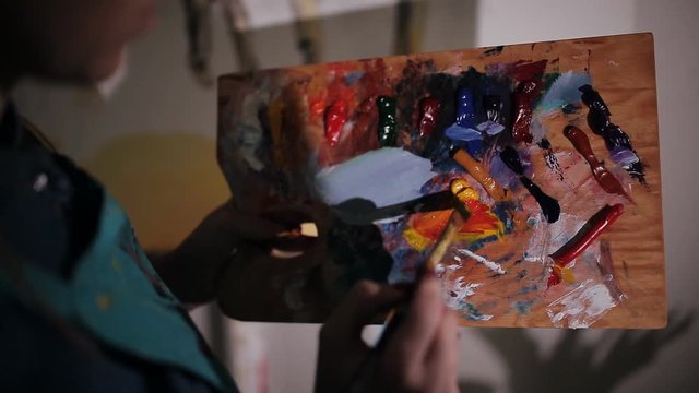 female artist mixes paint on the palette. close-up