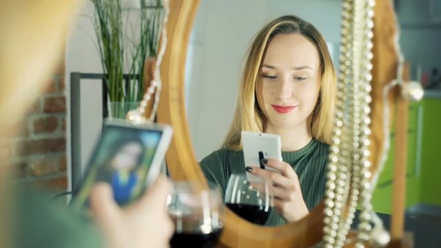 Happy girl sitting in front of mirror and browsing photos on smartphone
