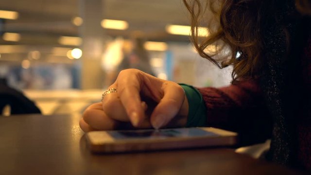 Closeup. Womans finger. Woman using smartphone in a cafe. Female shrolling internet and social networks. Smoothed peoples background