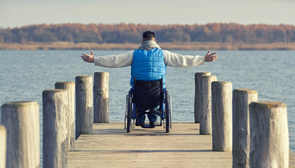 Mann mit Behinderung im Rollstuhl auf Steg am See