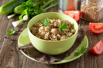 Buckwheat with meat stew and fresh vegetables on a wooden table.