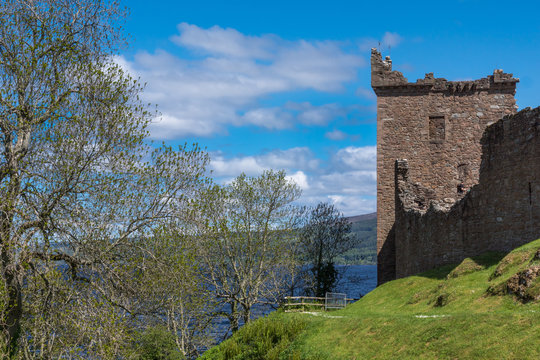 Loch Ness, Scotland - June 2, 2012: Shot of the main ruin, the tower of Urquhart Castle in combination with trees. Deep Blue Loch Ness visible in back. Green surrounding hills. Blue sky, white clouds.