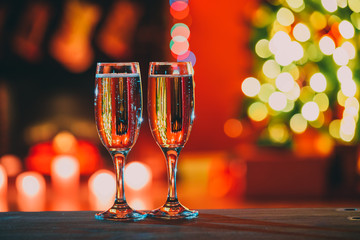 Beautiful two glasses of champagne standing on the table in the background of a blurred room with a decorated Christmas tree and fireplace. Soft focus. Shallow DOF