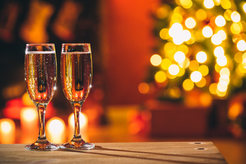 Beautiful two glasses of champagne standing on the table in the background of a blurred room with a decorated Christmas tree and fireplace. Soft focus. Shallow DOF