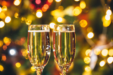 Beautiful two glasses of champagne standing on the table in the background of a blurred room with a decorated Christmas tree and fireplace. Soft focus. Shallow DOF