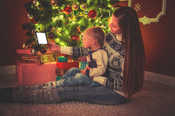 beautiful portrait of a little boy with his mother in a room with a Christmas tree by the fireplace looking at the tablet. Soft focus. Shallow dof
