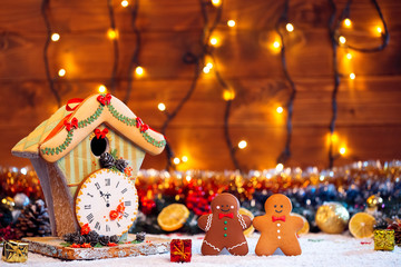 Christmas Gingerbread House with clock and two cookies man with fir festive decoration with snow on blurred bokeh background.