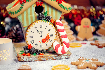 Christmas Gingerbread House with clock and candle with fir festive decoration with snow on blurred bokeh background.