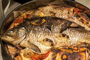 Roasted in oven carp fish on dough in pan with vegetables and lemons
