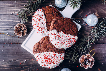 Homemade christmas chocolate cookies coated with white chocolate and candy canes sprinkles stacked on wooden table background. Christmas baking with festive