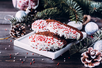 Homemade christmas chocolate cookies coated with white chocolate and candy canes sprinkles stacked on wooden table background. Christmas baking with festive