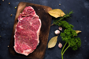 Raw steak with rosemary, salt and pepper cooking over stone table background