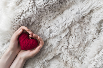 young woman is holding knitted red heart in her hands on fur coat