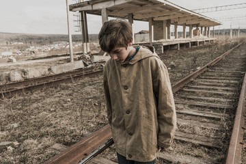 young boy goes rails near the abandoned train station. wandering boy. man in a protective cloak with a hood. Post apocalypse. traveling on foot in a post-apocalyptic world.