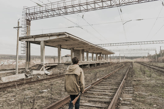young boy goes rails near the abandoned train station. wandering boy. man in a protective cloak with a hood. Post apocalypse. traveling on foot in a post-apocalyptic world.