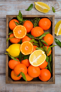 Fresh tangerine clementine and lemons with leaves in wooden tray on wooden background, top view, vertical.