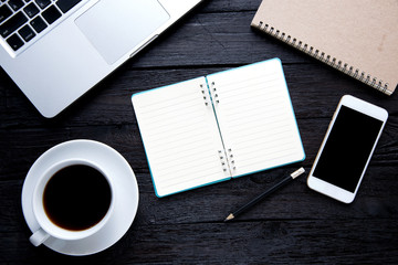 Office desk table with computer, supplies, coffee cup and mobile on dark wooden table background
