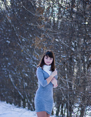 Pretty girl in a gray dress standing in a snowy park