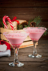 Traditional Christmas pink cocktail candy cane punch in glasses, decorated with shards of candy cane. Against box with gifts, the Christmas tree branches and decorations, copy space