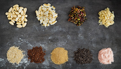 Obraz na płótnie Canvas Various superfoods and nuts on a dark grey background. Quinoa, flex seeds, amarant, chia seeds, rose salt, blanched almonds, shredded coconut, pistachio, almond slices. Horizontal, copy space