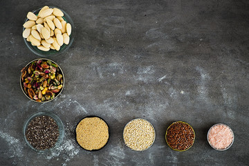 Various superfoods and nuts on a dark grey background. Slivered almonds, pistachios, chia seeds, amarant, quinoa,  flex seeds, rose salt. Copy space for text