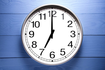 Round clock shows shows at 7 o'clock, clock on blue background