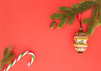 Christmas frame on red background. Green fir branches, Xmas decoration and candy cane. Top view, flat lay. Copy space for text