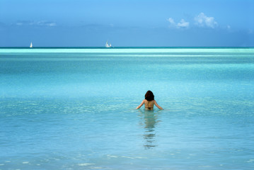 Woman walking into calm ocean waters in tropical island beach scene
