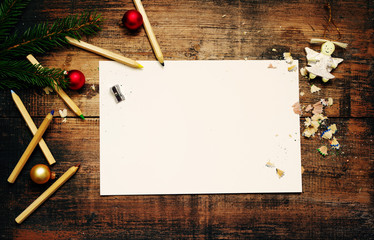 Empty clean sheet of paper for your inscription, pencils and Christmas decorations on a wooden surface. Concept of New year and Christmas. Top view
