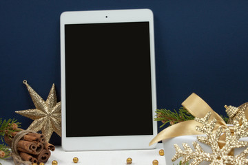 Digital tablet with Golden christmas decoration with golden snow flake, cinnamon, pine branches, golden ball and golden ribbon on white wood background