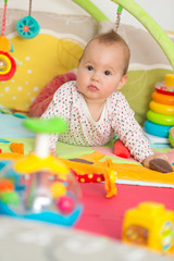 Fototapeta premium Eight months old baby girl playing with colorful toys on a floor