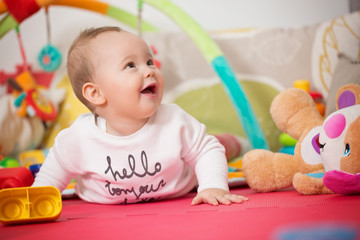 Eight months old baby girl playing with colorful toys on a floor