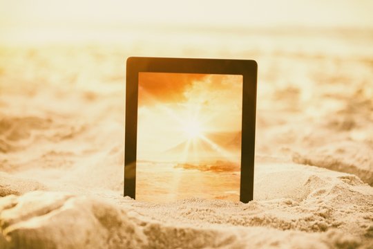 Composite image of digital tablet kept on sand