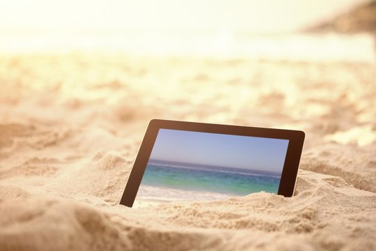 Composite image of digital tablet kept on sand at beach