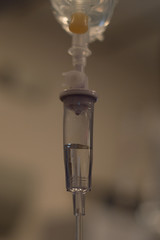 Close Up of Intravenous Drip Chamber partially filled with clear fluid and a fluid drip suspended at the top.