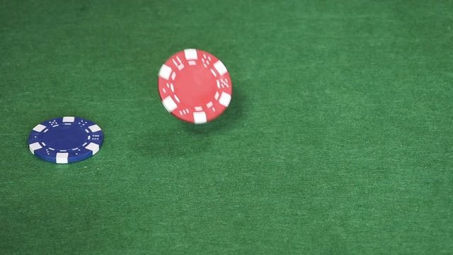 Red, blue, black and green gambling poker chips fall on empty green table, casino games, poker tokens scattered on table. Close up, slow motion.