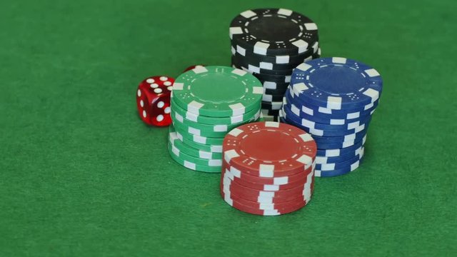 Four sets of blue, green, red, red poker chips and two red dice with six on both rotating on casino table, gambling. Close up, seamless loop, 4K Ultra HD.