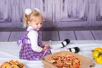 The child, a little girl sitting on the floor and having fun eating pizza. Unhealthy diets.