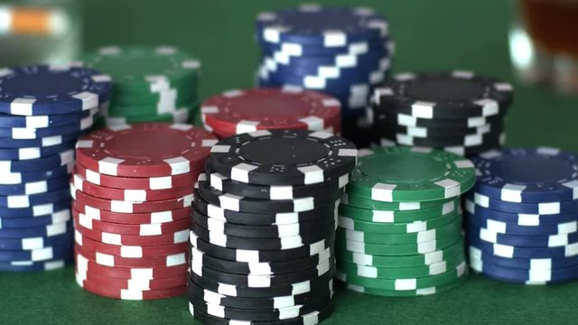 Player puts back on table glass with drink and reaches out to grab poker chips, concept of victory, playing card games, gamble. Close up, shallow DOF, 4K Ultra HD.