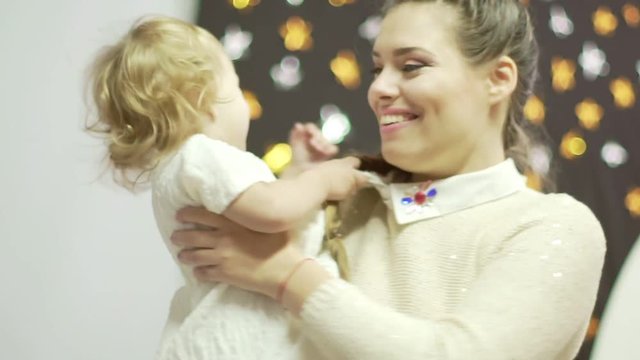 Happy mother and her little daughter go round in a decorated room with lights