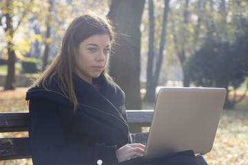 Young business woman with the laptop sits on a bench in the park